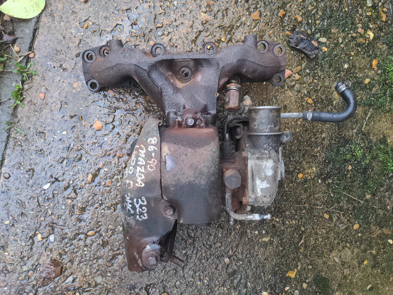 An IHI VJ9 turbo attached to an exhaust manifold. The parts that are not corroded are oily. It is as worn-out as it looks