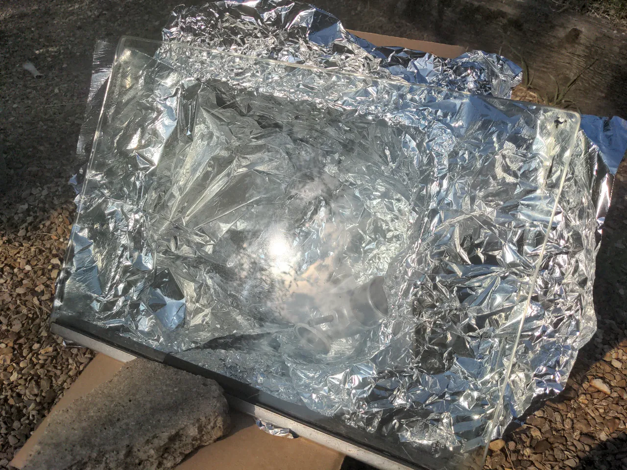 My pipe baking in a home-made solar oven; it is a cardboard box lined with foil and a sheet of Land Rover glass over it. A reflection of the sun shows that it is a very sunny day.