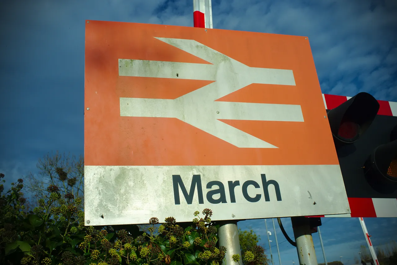 A standard British station sign: a Double Arrow symbol in white against a flame red background, with the name of the station (March) written underneath.