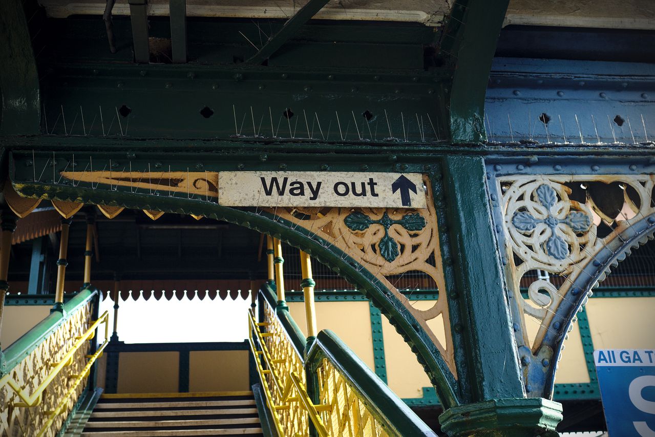 A "Way out" sign, with a thick directional arrow, indicating that one should head up the footbridge in the photo.
