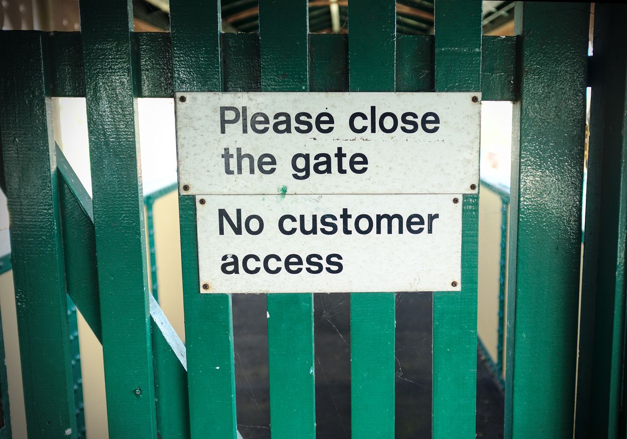 A gate with two signs: "Please close the gate" and "No customer access".