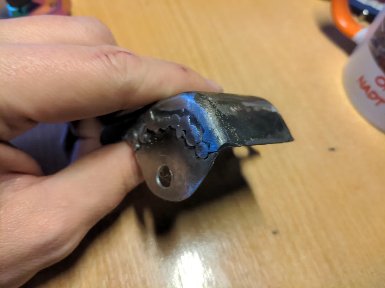 A wastegate actuator heat shield. It has a section cut out, and a new section welded in its place with a hole in it for a bolt.