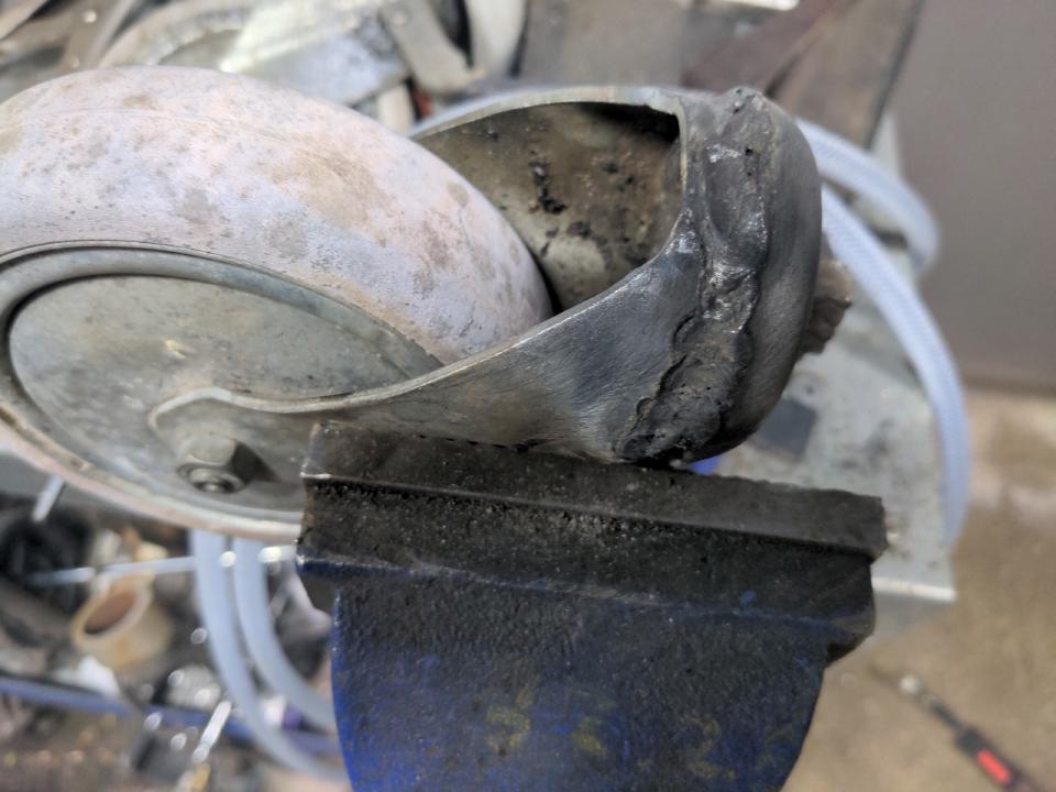 A castor wheel in a vice on my workbench, crudely welded up to make it non-swivelling.