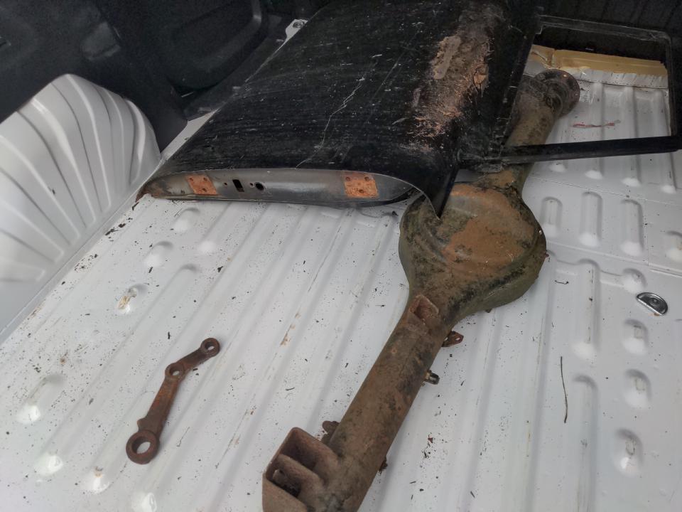 The load bay of my rented van, showing an axle housing, a steering component, and a black door that is not in very great-looking condition.