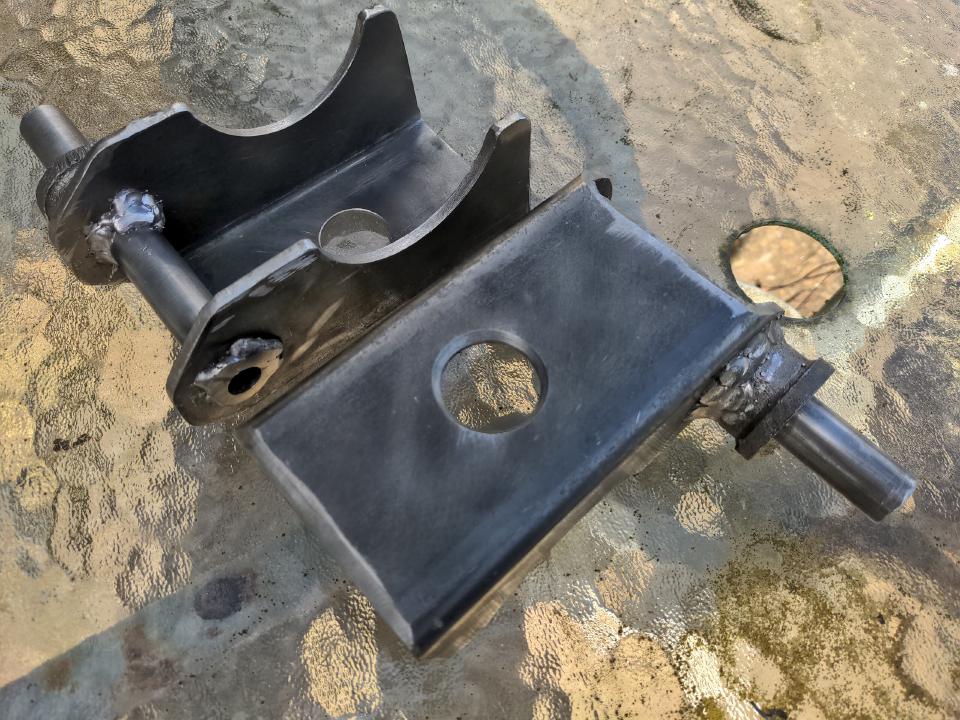 A photo of my home-made leaf spring mounts made from my starting point of some 80x80x3mm box section steel and some 19mm steel tube. These weld on to the axle at one side (and have a 3-inch-diameter round cut-out for it), and sit on the leaf spring on the other, with a counter-sunk 29mm locating hole. The tube pushes through holes and protrudes on one side to give the shock absorber something to mount to.