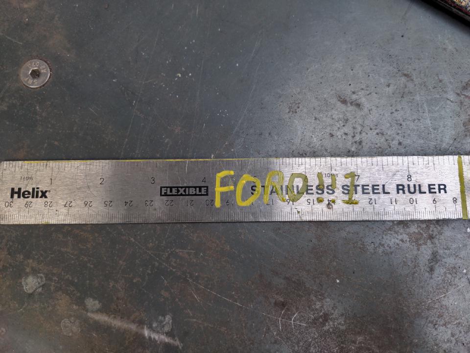 A metal ruler, with a mark at the 9 inch point, and "FORD!!1" written on it.