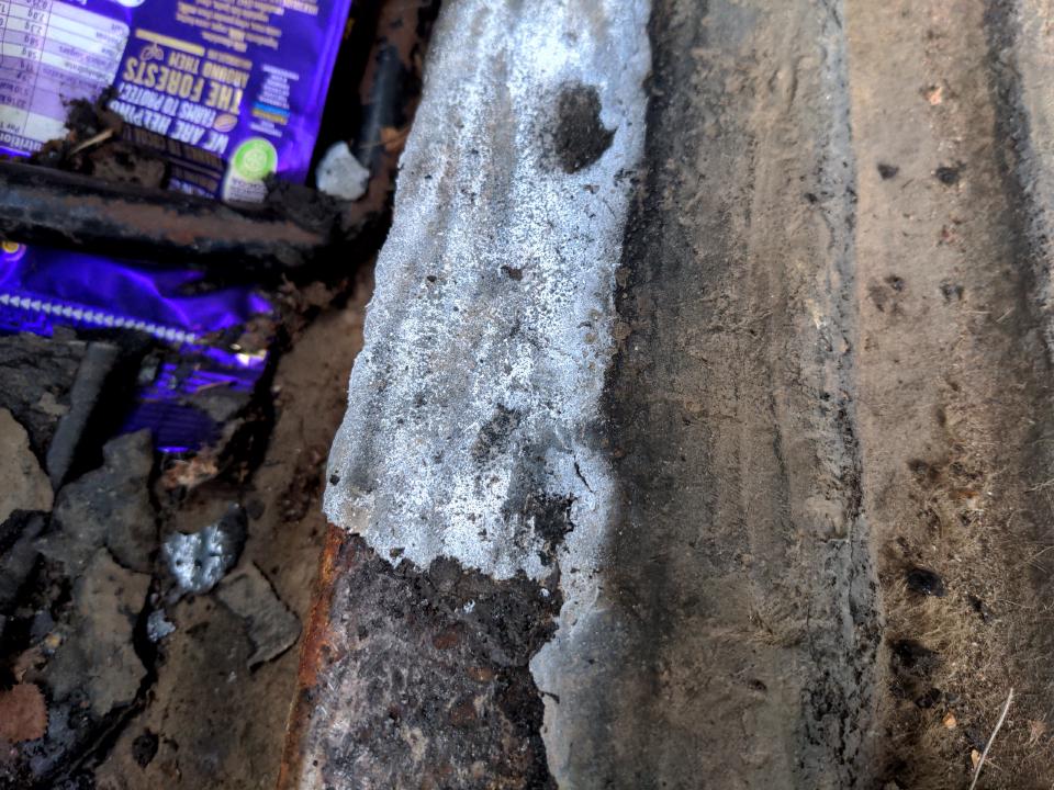 An area of the bituminous paint in the boot of my car after being sprayed with aerosol freeze spray; it has turned white. An area of bare steel just below it shows where I have been chipping the paint off using this method.