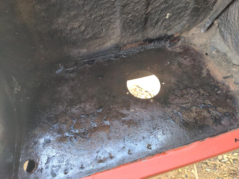 A view into the floor area behind the rear wheel arch of my Rover P5. It is slightly glossy raw steel because it has been coated with Jenolite rust eater. It has a roughly two-inch wide hole as a drain.