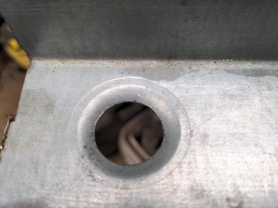 The same piece of scrap steel, after the hole has been tickled with a dimple die. It causes the hole to be pushed outwards and a larger circle to be pressed in around it. Think the shape of a funnel.