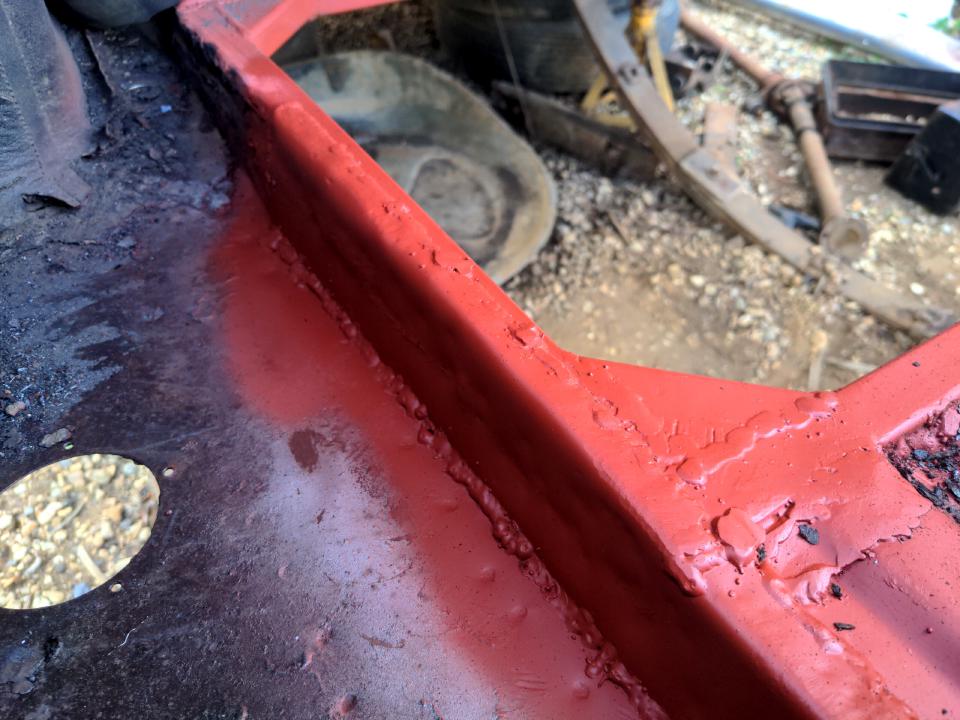 A repair in the boot of my Rover P5. Where the boot floor was is now a massive hole (for the radiator) lined with 1 inch box section steel. A section of metal has been welded in (fairly crudely, hence the "I know") around the edge of this box section; this replaced a piece that was rotten. The area is sprayed in red anti-rust primer.