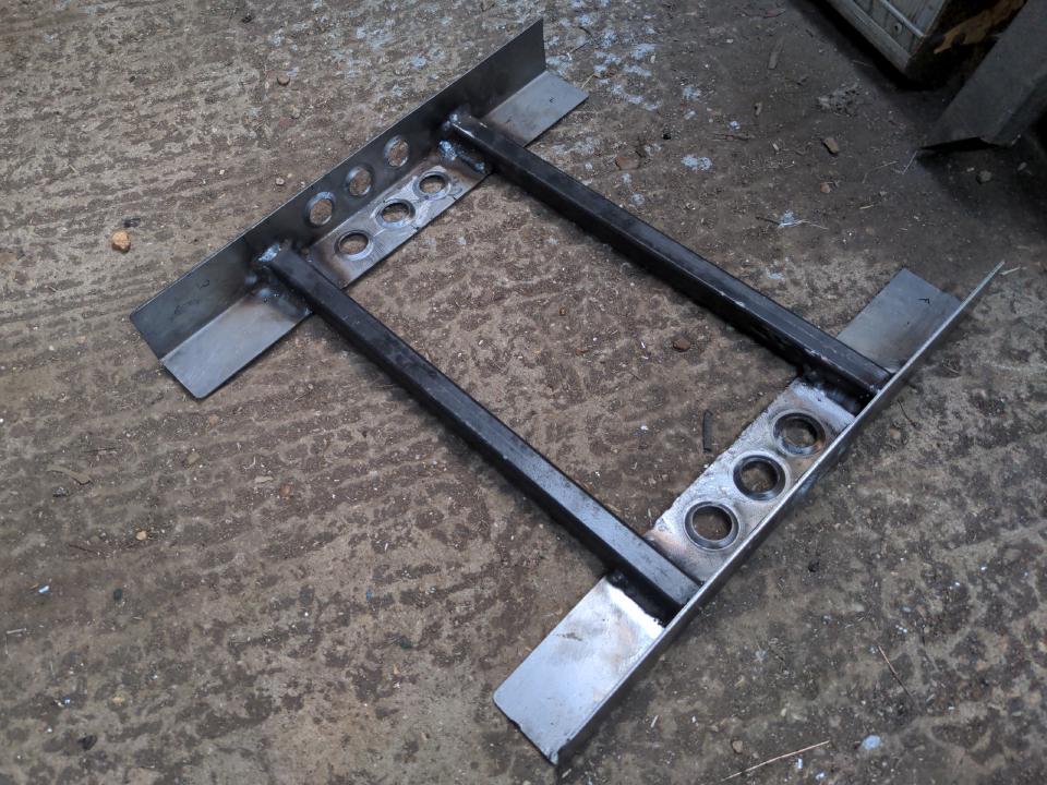 The start of a subframe for mounting the Supra seat to something that isn't a car. It is 2 lengths of 50x50x2mm angle iron, spaced apart by about a foot and a bit of 20x20mm box section steel. Each angle section has 6 dimpled holes for weight saving.