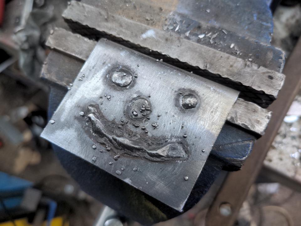 A crude face drawn onto some steel with a welder.