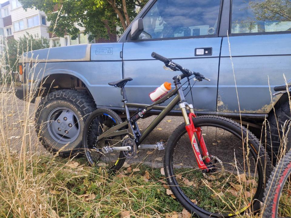 A grey early 2000s Marin full suspension mountain bike sitting in front of an 80s light blue Range Rover.