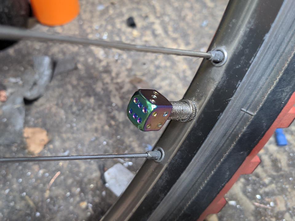 A dust cap fitted to one of my bicycle's tyre valves. They are shaped like small dice. They are metal with a rainbow-anodised finish.