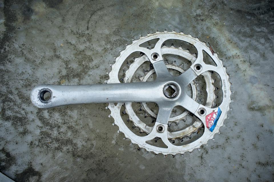 A Sugino Super Shifter Pro chainset. It is a three-ring five-arm crank and it is all silver. It needs a clean.