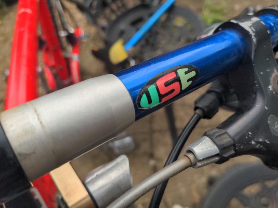 Blue anodised USE bars; a close up of the USE sticker is in shot. A shim from the small handlebar to the much larger stem clamp is visible.