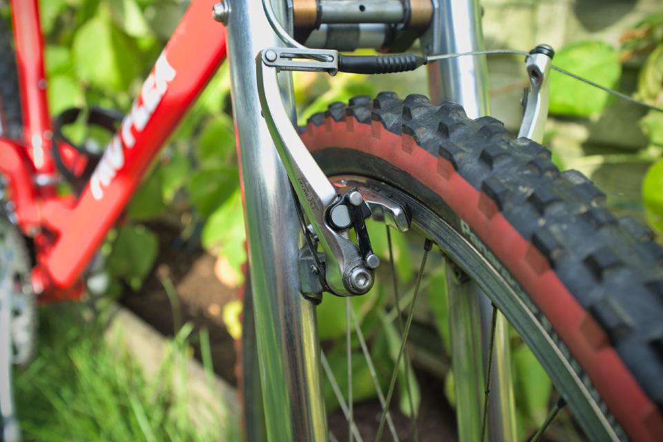 One of the arms of some Shimano XT V-brakes. They are silver with subtle black writing. They have a mechanism that ensures that the pads push flat on to the rim, rather than moving in an arc like the arms do.