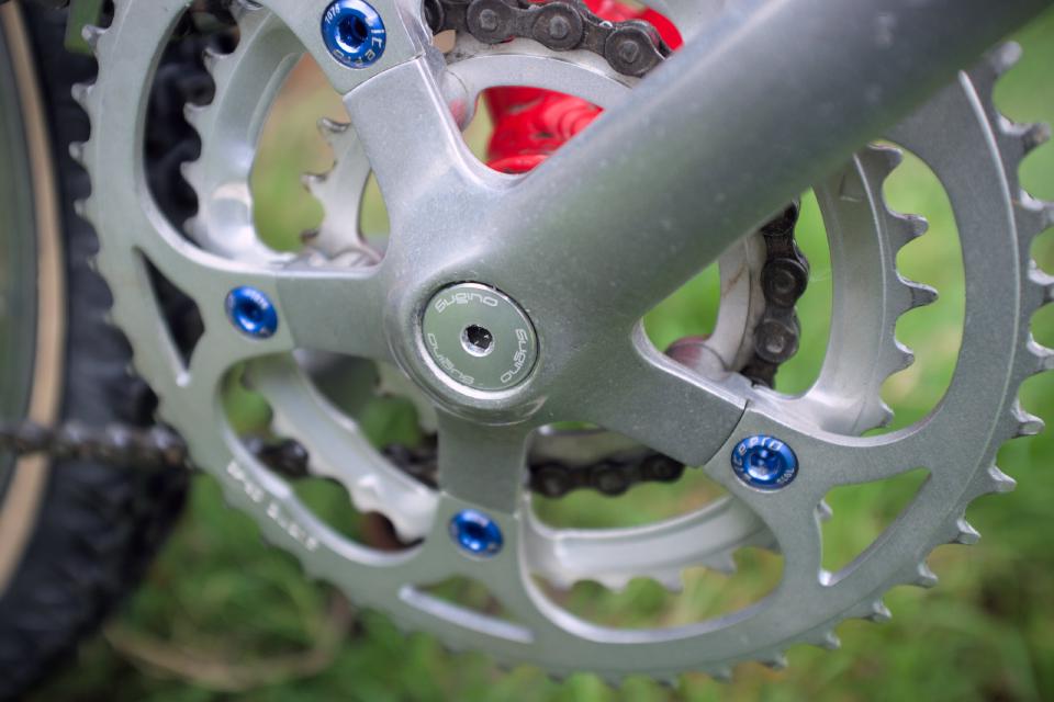 A close up of some Sugino dust caps on some Sugino cranks; they are silver with white writing.