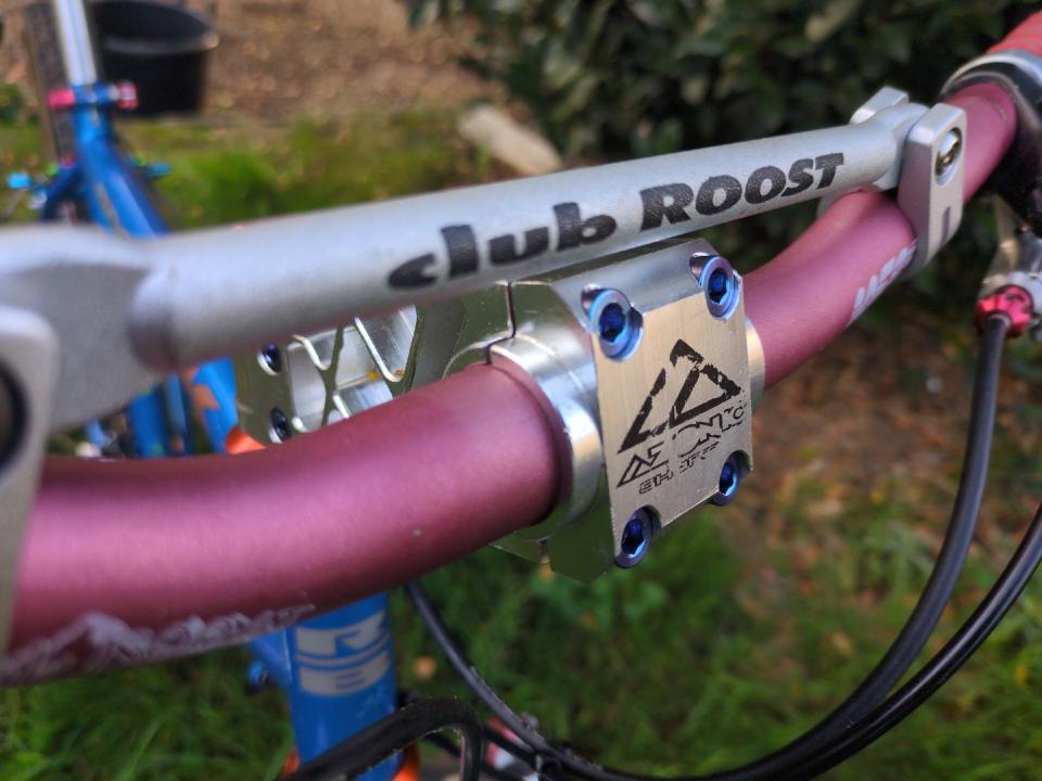 A closeup of the stem area on some red Club Roost bars, with a silver Azonic CNC stem, a silver brace, and super-fancy titanium bolts.