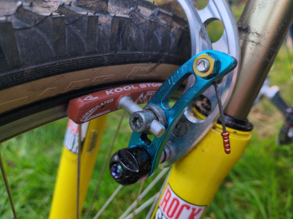 Close up of one of my front cantilever brakes. They are blue and the visible bolt has a gold head.