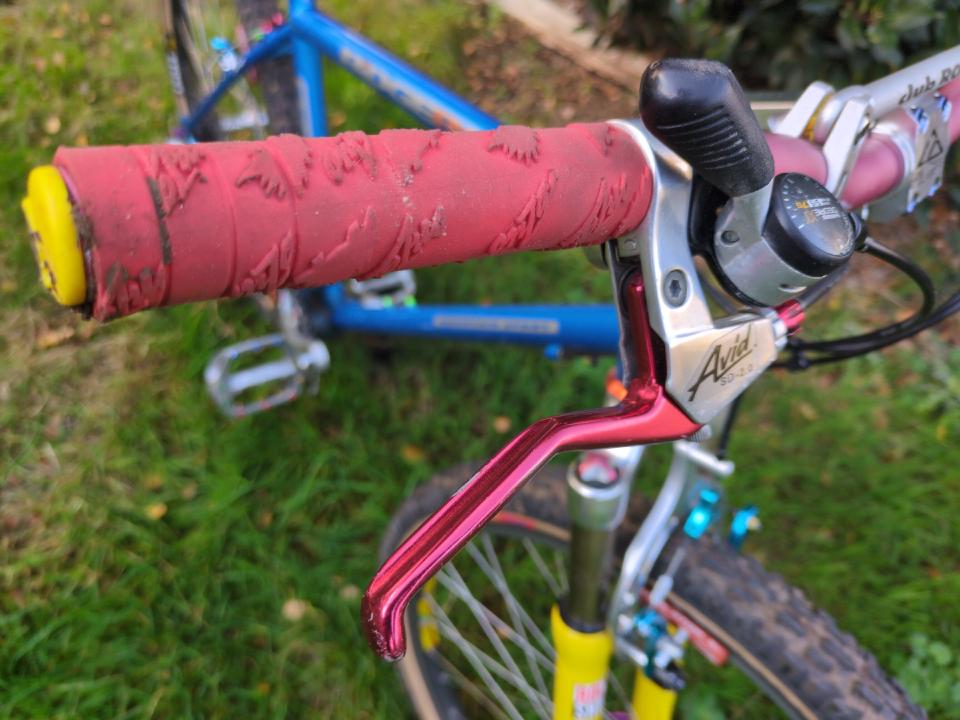 A close up of my controls of the bike with XT thumbshifters, slightly dirty red grips, and some silver brake levers with red handles.