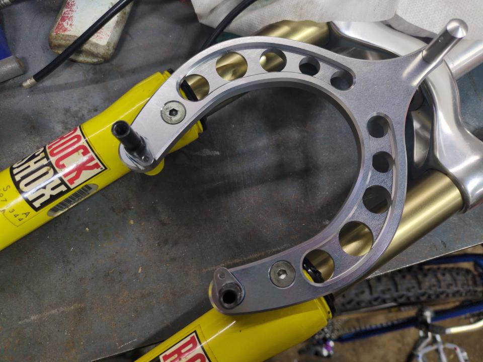 The arch (component joining the two fork legs together via the rim brake attachment points) for the Judy SL forks. It is polished silver.