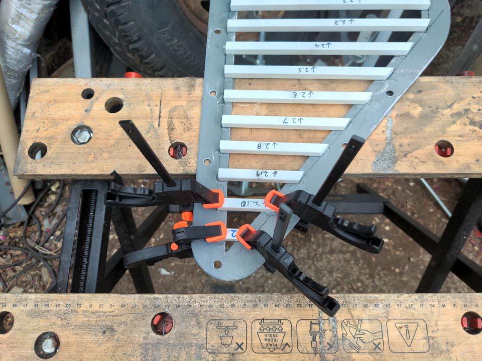 Across the short dimension of the right angle triangles, following the same right angle, I have glued 12 lengths of 10mm white plastic ABS square tubing. One of them is clamped into place in the photo.