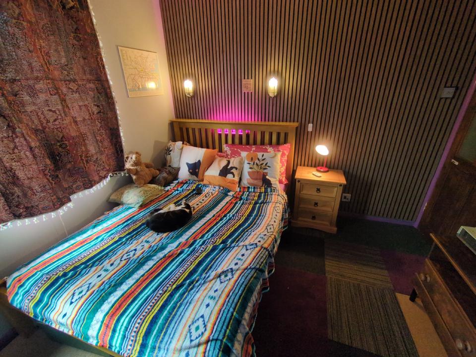 The end of my bedroom project; a large double pine bed, random-coloured carpet tiles, a wood slat feature wall, bulkhead lights, and very colourful coverings.