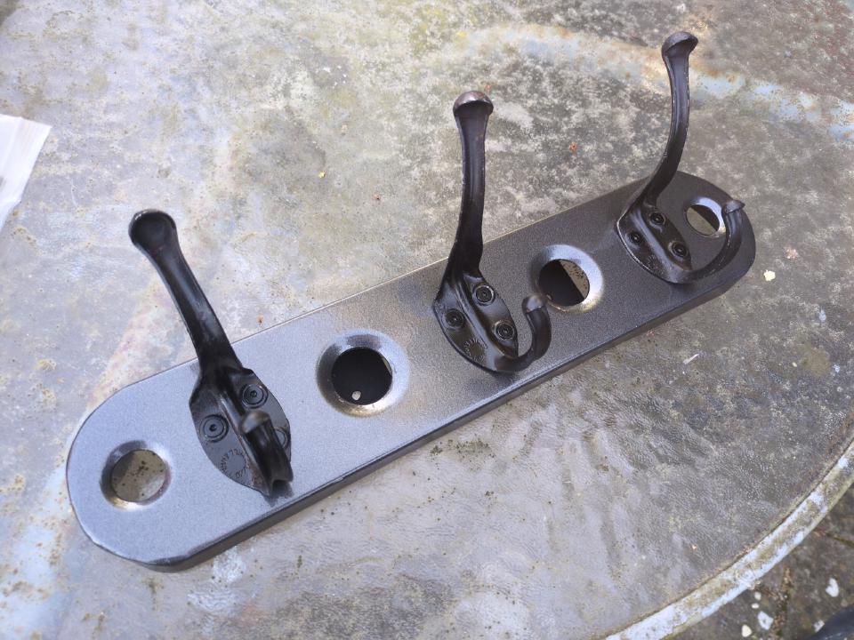 A piece of dimpled steel acting as a backing plate for three coat hooks.
