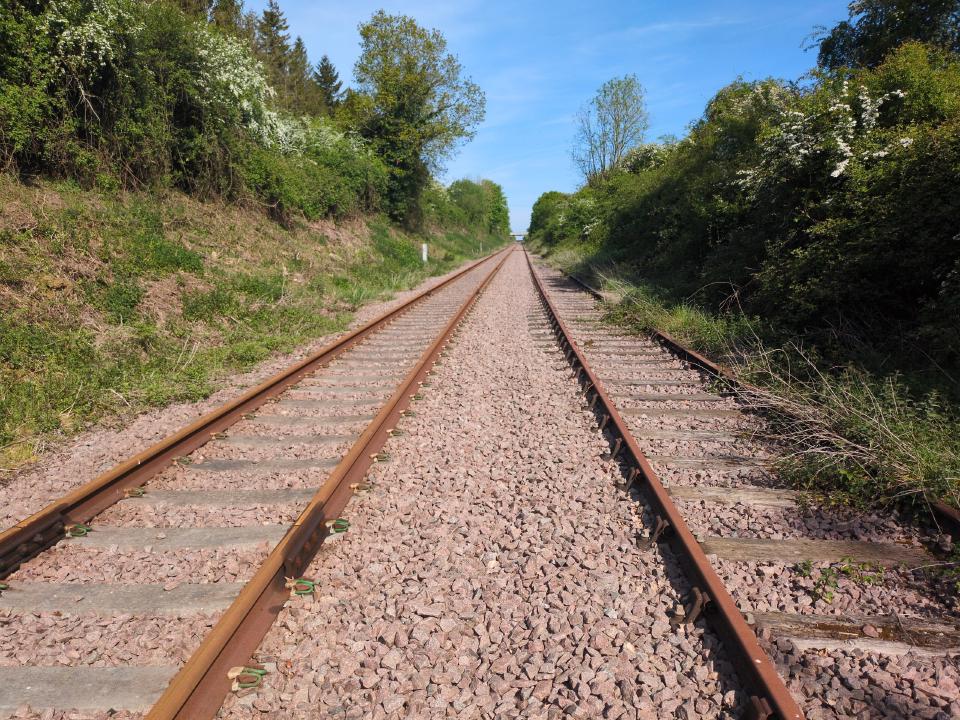 A view down some rural railway tracks, with embankments either side, on a blue-skied day.
